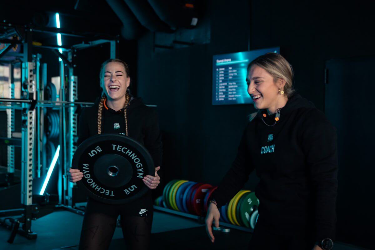 Zwei Personaltrainerinnen lachen beim Verräumen von Technogym Gewichten im King Kong Club Salzburg.